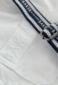 Biały materiał z wytłoczonym logo "BAKER". Posiada granatowy, tkany pasek z białym paskiem i metalową klamrą, podkreślający swobodny styl.