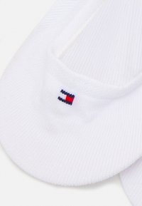 Hvide ankelstrømper med ribbet tekstur, der har et lille blåt, rødt og hvidt logo på kanten.