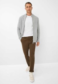 Cardigan en tricot gris sur un T-shirt blanc, associé à un pantalon marron et des baskets crème. Le cardigan a un col et des poignets côtelés.