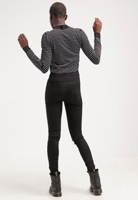 Musta-valkoraidallinen vartalonmyötäinen neule, jossa on resorireunukset hihoissa ja helmassa, yhdistetty tiukkoihin mustiin farkkuihin ja mustiin nilkkureihin, joissa on kultaiset yksityiskohdat.