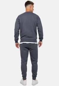 Grijze sweatshirt en joggingbroek van zachte stof, met ribbels aan de mouwen en tailleband, gestyled met een wit T-shirt eronder en witte sneakers.