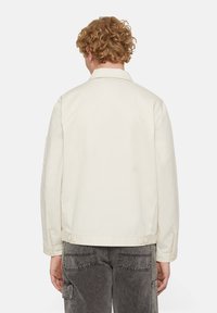 Light beige jacket with a collared neck, long sleeves, and buttoned cuffs. Smooth texture, simple design, no visible patterns or accents.