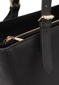 Zwarte leren handtas met een gestructureerde afwerking, verstelbare schouderriem, gouden hardware en een ritszak met een merketiket.