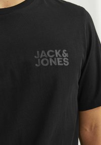 Schwarzes Baumwoll-T-Shirt mit einem subtilen, dunkelgrauen "JACK & JONES"-Logo auf der Brust. Klassischer Rundhalsausschnitt, kurze Ärmel.