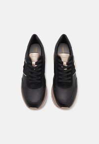 Paired de baskets noires avec des accents beiges, des lacets et des semelles intérieures de marque, vues de dessus sur un fond blanc.