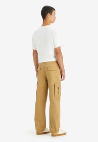Tan cargo pants made of durable fabric, featuring side pockets, a relaxed fit, and a white t-shirt with short sleeves. Plain design.