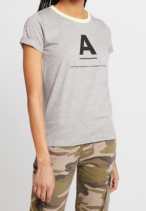 Szary t-shirt z krótkim rękawem z żółtym prążkowanym dekoltem, na przodzie z wyraźną czarną literą "A" i tekstem poniżej. Casualowy krój.