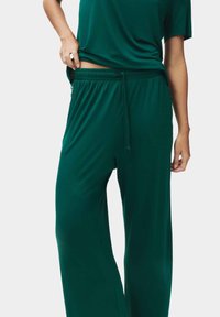 Groene, loszittende loungebroek gemaakt van een zachte, elastische stof. Kenmerkt zich door een elastische tailleband met een trekkoord en zijzakken.