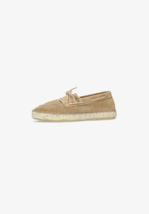 Tan suède mocassinstijl schoen met vetersstrik en gevlochten jute zool, gezien van opzij op een witte achtergrond.