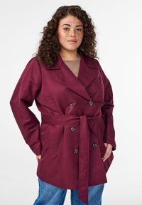 Bordeauxfarbener doppelseitig geknöpfter Mantel mit tailliertem Gürtel, großen Knöpfen und Seitentaschen. Hergestellt aus glattem Stoff mit maßgeschneiderter Passform.