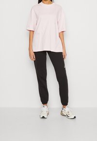 Rosa oversized t-shirt med korta ärmar, svarta tapered sweatpants och vita sneakers med multicolor-accenter.