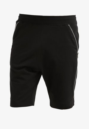 T-shirt noir à col en V, short de sport noir avec un détail zippé, et baskets noires. Porte un sac de sport noir avec des poignées grises.
