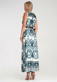 Długa, bezrękawnikowa sukienka z białego materiału ozdobiona niebieskim i turkusowym wzorem w ornamenty, z dopasowaną talią i kontrastującym brązowym paskiem.