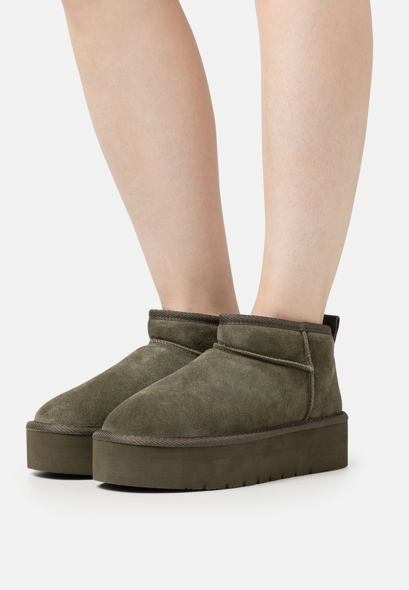 Olive green ankle boots made of suede, featuring a rounded toe, sturdy platform sole, and simple stitching along the edges.