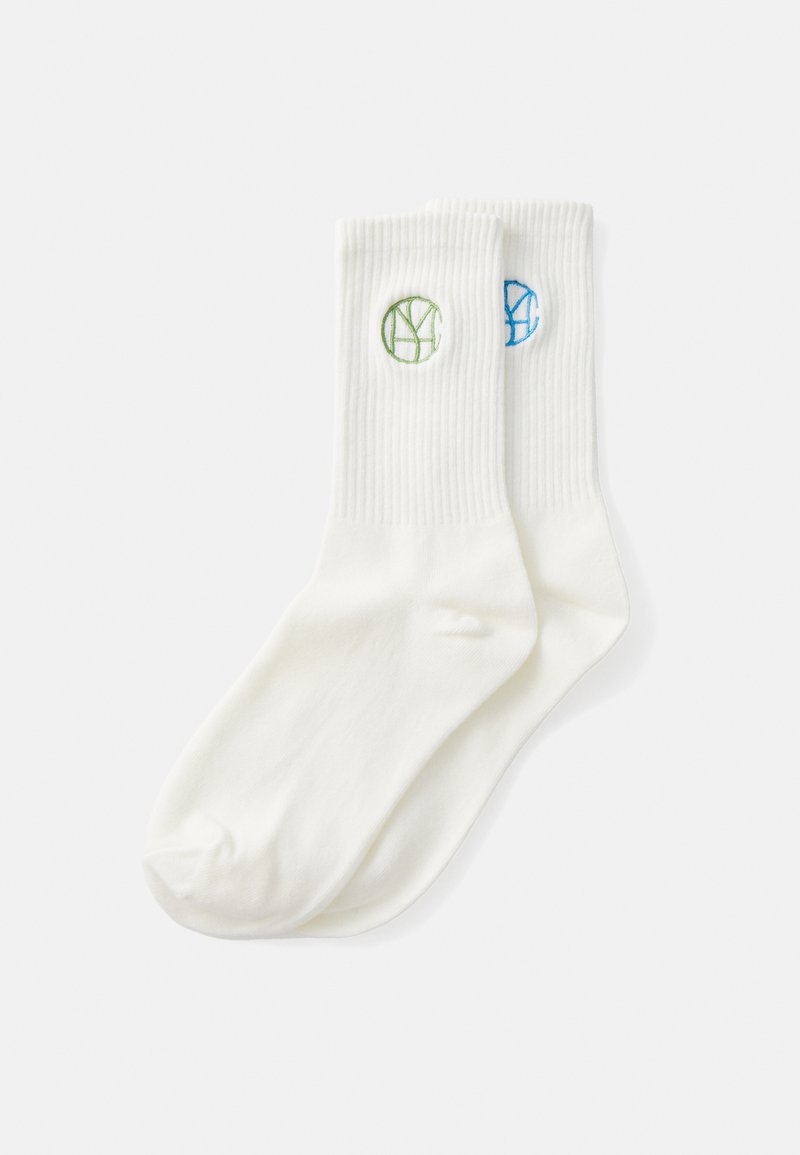 Chaussettes en coton blanc avec une texture côtelée. Présentent des logos circulaires brodés verts et bleus sur le côté supérieur.