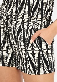 Šortky s černobílým vzorem a designem listů, vyrobené z měkké látky, s elastickým pasem a postranními kapsami.