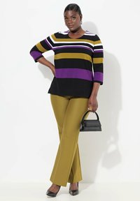Randig topp i flera färger, svart, lila och guld, med trekvartslånga ärmar, i kombination med olivgröna utsvängda byxor och en liten svart handväska.