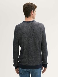Pull en maille marine avec motif texturé, col rond, et poignets et ourlet côtelés. Détails de couture visibles et coupe décontractée.