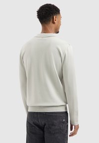 Hellgrauer Sweatshirt aus strukturiertem Material mit gerippten Bündchen und Saum. Verfügt über einen klassischen Kragen und eine lässige Passform, kombiniert mit dunkler Jeans.
