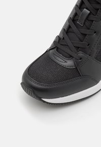 Černá sportovní bota s texturovaným látkovým svrškem, hladkými koženými doplňky, tradičním šněrováním a bílou gumovou podrážkou.