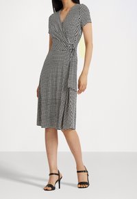 Czarna i biała sukienka w kratkę, zapinana na krótkie rękawy, z dekoltem w kształcie litery V i wiązaniem w pasie. Noszona z czarnymi sandałami na wysokim obcasie z paskami.
