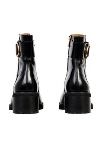 Botines de cuero negro con un acabado brillante, tacones cuadrados y un acento circular dorado cerca del tobillo. Cierre de cremallera en la parte posterior.