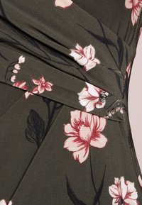 Látka s květinovým vzorem v olivově zelené barvě, s růžovými a bílými květinami, s texturovaným povrchem a sklady v designu.