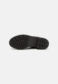 Suela de bota de goma negra con patrón de tacos profundo, acabado texturizado y sección del talón reforzada. Sin marcas de marca visibles ni acentos.