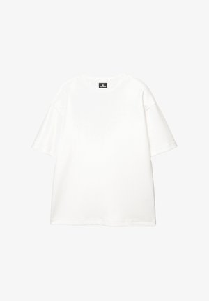 Bela bombažna majica s krožnim izrezom, kratkimi rokavi, sproščenim krojem in minimalnimi šivi. Gladka tekstura in čist dizajn.