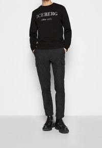 Felpa nera con la scritta "ICEBERG since 1974" in bianco, abbinata a pantaloni cargo scuri e stivali neri stringati, con una vestibilità slim.
