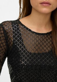 Zwarte mesh top met een ruitpatroon, versierd met pailletten. Heeft een ronde halslijn en lange mouwen, wat zorgt voor een doorschijnend stofeffect.