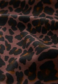 Gros plan sur un tissu doux avec un motif léopard marron foncé et noir, montrant la texture et les plis.