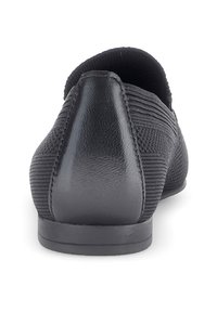 Black slip-on shoe with textured fabric, smooth leather heel, and a low, flat sole. Features a subtle vertical ribbed pattern.
