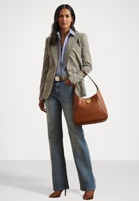 Ruda odinė petinė rankinė su apvalia forma ir auksiniais aksesuarais. Modelis vilki languotą švarką, dryžuotą marškinį ir išsiplėtusias džinsus.