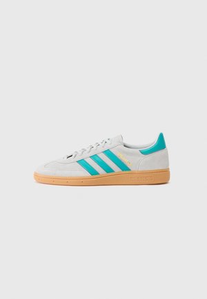 Baskets blanches Adidas avec des bandes bleu sarcelle et languette de talon, semelle en gomme, texte doré "SPEZIAL" sur le côté, montrées de profil droit sur fond gris.