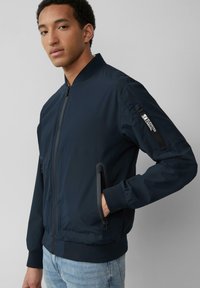 Marine bomberjack met een rits aan de voorkant, geribde manchetten en zijzakken. Voorzien van een mouwzak met een logo patch. Glad, lichtgewicht materiaal.