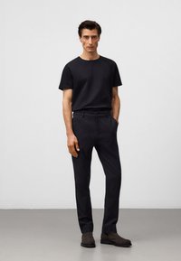 Czarny t-shirt z okrągłym dekoltem zestawiony z ciemnymi, eleganckimi spodniami. Materiał wydaje się gładki, z luźnym krojem i subtelną fakturą. Ciemne botki dopełniają całość.