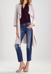 Ljusgrå lång cardigan över en mörklila topp, kombinerad med slitna blå jeans och blekgra höga klackar.