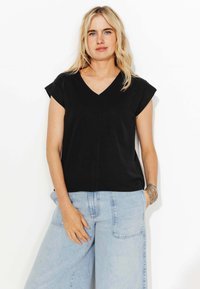 Haut noir à col en V avec des manches courtes, en tissu doux. Assorti à un jean bleu clair à jambe large, mettant en avant une coupe décontractée et confortable.