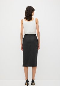 Sort blyantskirt med en tætsiddende design, knælang, subtil tekstur og en slids bagpå. Sammen med en simpel ærmeløs hvid top.
