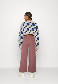 Sweater curto com um padrão xadrez multicolorido em roxo, verde, azul e preto. Combinado com calças largas em burgundy e sapatos brancos.