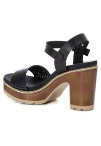 Sandalias de tacón de cuero negro con un diseño de tira perforada, un tacón grueso marrón y una suela de goma de color claro con detalles de costura.
