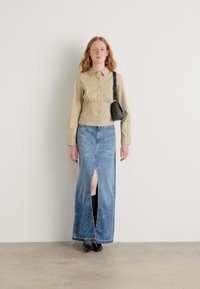 Beige pamut ing, gyűjtött részletekkel, kék denim maxi szoknyával párosítva, amely elöl hasítással és átlós varrással rendelkezik. Fekete kiegészítők.