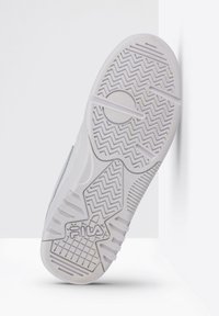 Suela de zapatilla blanca con patrón de tracción en zigzag, superficie texturizada y emblema circular. Hecha de goma con acentos duraderos.