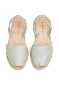 Sandalias de cuero gris claro con suela plana, diseño de punta abierta y correas ajustables en los tobillos; presentan costuras en contraste y plantilla suave.