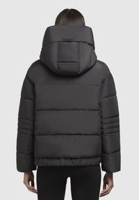 Giacca a vento nera con una grande cappuccio, design trapuntato, polsini elasticizzati e vestibilità cropped. Il tessuto appare liscio e leggero.