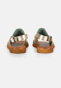 Sandalias metálicas doradas con un talón descubierto, correas de cuero y hebilla ajustable. Suela texturizada marrón con forro interior azul.