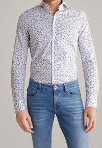 Wit overhemd met blauw vogelpatroon, knoopsluiting aan de kraag, lange mouwen; gecombineerd met lichtblauwe denim jeans met subtiele vervaging.