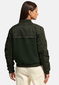 Tmavozelená bomber bunda s vypchávkovaným telom a saténovými rukávmi, rebrovanými manžetami a švom na chrbte.