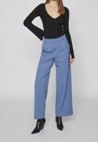 Czarna prążkowana bluzka z długim rękawem i dekoltem w serek, w połączeniu z jasnoniebieskimi szerokimi spodniami. Całość uzupełniają czarne botki na obcasie. Gładka struktura materiału.